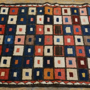 Geometric high-pile rug with navy, red, cream, and brown checkerboard squares on wood planks.