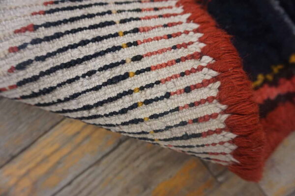 Close-up of a rolled rug showing red, navy, and yellow woven stripes on a light structure over wood flooring.