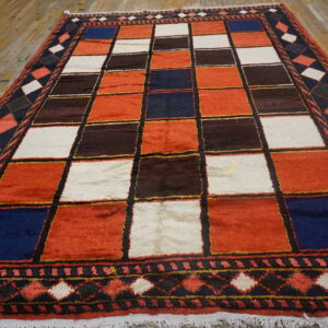 Geometric rug with rust, white, navy, and brown squares and dark patterned borders on wood flooring.