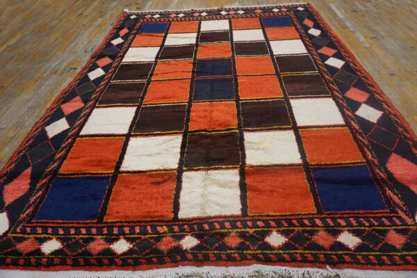 Geometric rug with rust, white, navy, and brown squares and dark patterned borders on wood flooring.