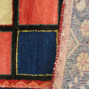 Geometric rug pattern of red, blue, and beige blocks with black borders, viewed beside the woven backing.