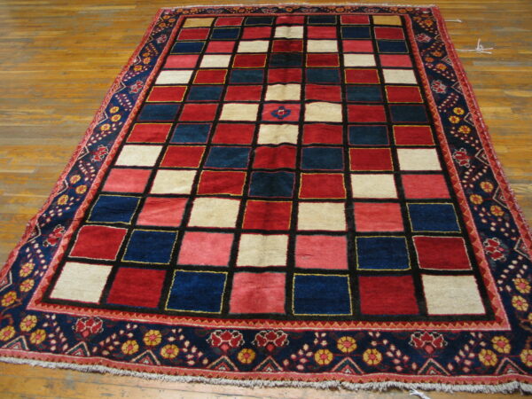A red, navy, and cream checkered rug with a detailed border rests on wood plank flooring.