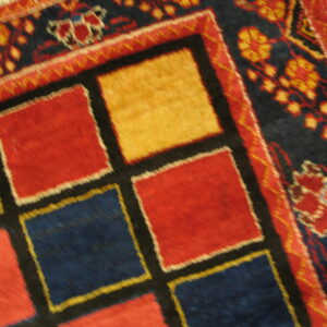 Geometric high-pile rug with central red, blue, and yellow squares next to a detailed floral border on wood flooring.