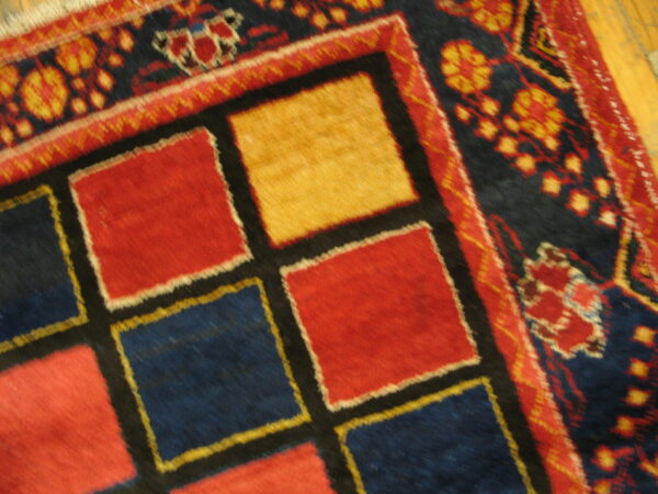 Geometric high-pile rug with central red, blue, and yellow squares next to a detailed floral border on wood flooring.