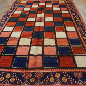 Geometric red, navy, and cream checkerboard rug with patterned floral outer border on wood flooring.