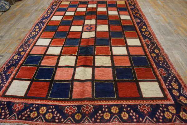 Geometric red, navy, and cream checkerboard rug with patterned floral outer border on wood flooring.