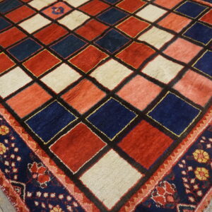 Red, navy, and cream diamond-pattern rug with a thick floral border rests on light wooden floors.