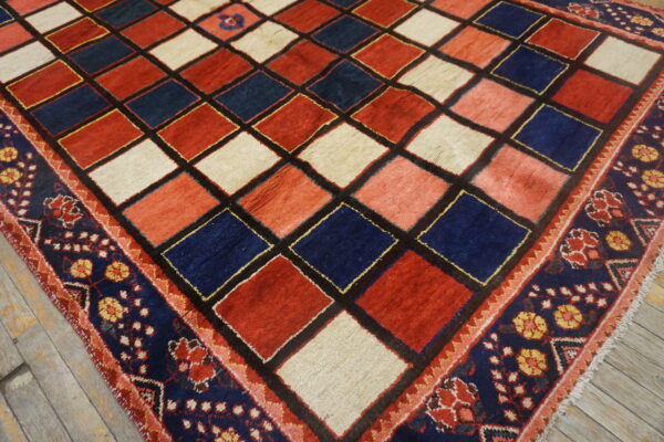 Red, navy, and cream diamond-pattern rug with a thick floral border rests on light wooden floors.