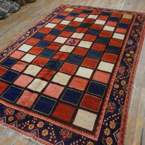 Red, blue, and cream checkerboard rug with a detailed navy border rests on distressed wooden floorboards.