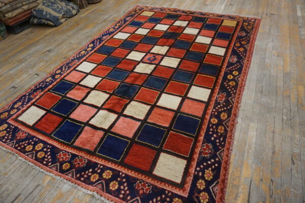 Red, blue, and cream checkerboard rug with a detailed navy border rests on distressed wooden floorboards.