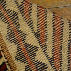 Detailed view of a beige, red, and black zigzag pattern rug lying on distressed wood floorboards.