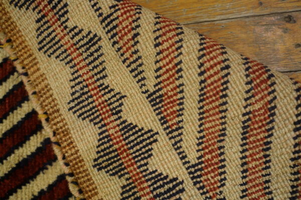 Detailed view of a beige, red, and black zigzag pattern rug lying on distressed wood floorboards.