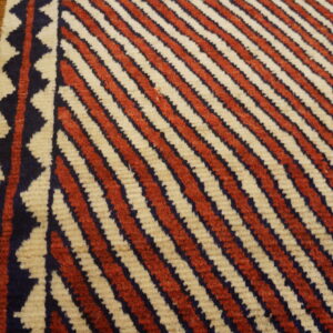 Red and cream diagonal stripes meet a navy zig-zag border on a distressed wood floor.