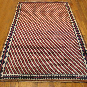 Red and cream diagonally striped rug with a dark blue geometric border on wood flooring.