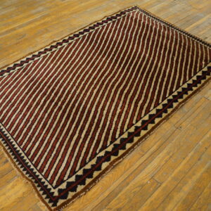 Low-pile rug with diagonal reddish-brown and tan stripes features black zigzag borders on rustic wood planks.