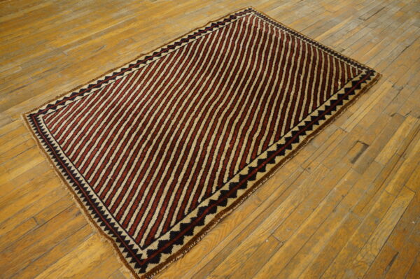 Low-pile rug with diagonal reddish-brown and tan stripes features black zigzag borders on rustic wood planks.