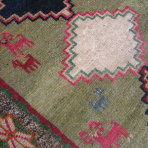 Geometric rug detail showing green ground, zigzag borders, cream panels, and red and blue stylized motifs.
