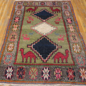 Traditional olive rug featuring stepped diamonds and red animals, framed by a colorful geometric border on wood.