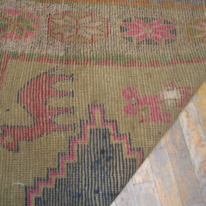A corner of a muted khaki and red flatweave rug with geometric designs rests on distressed wooden floors.