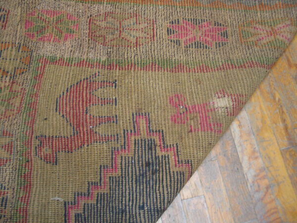 A corner of a muted khaki and red flatweave rug with geometric designs rests on distressed wooden floors.