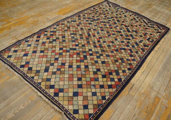 Multicolor checked diamond rug with a dark border lying on rustic, worn wood planks.