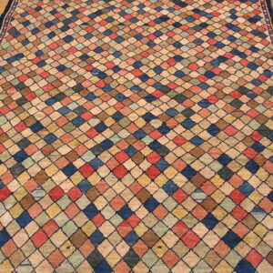 Multicolored diamond-patterned rug in blue, red, beige, and yellow rests on a wooden plank floor.
