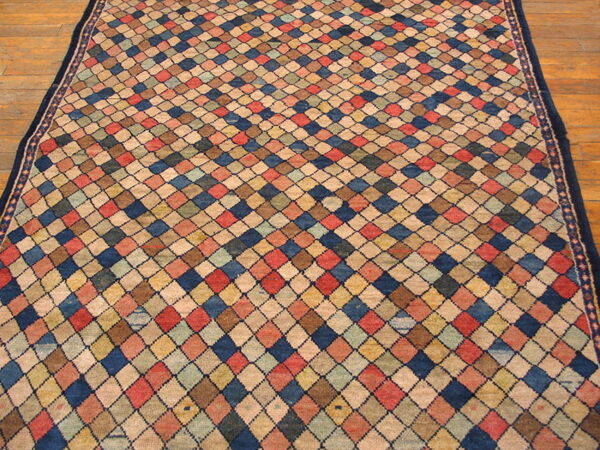 Multicolored diamond-patterned rug in blue, red, beige, and yellow rests on a wooden plank floor.