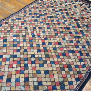 Low-pile rug with a textured mosaic pattern in blue, pink, cream, and brown on wood planks.