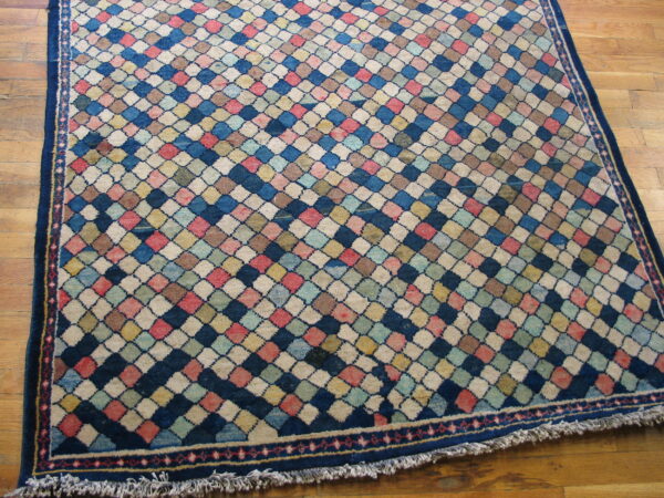 Medium pile rug with a variegated diamond pattern in blue, pink, cream, and yellow on a wood floor.