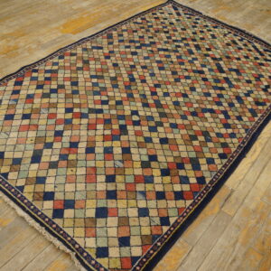 Multicolored checkered rug with a navy border is centered on worn wooden flooring.