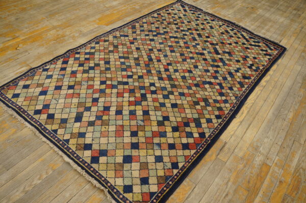Multicolored checkered rug with a navy border is centered on worn wooden flooring.