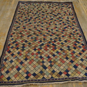 Low-pile rug with multicolored diamond trellis pattern and a dark blue border on distressed wood floor.