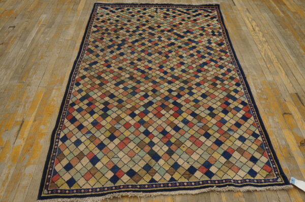 Low-pile rug with multicolored diamond trellis pattern and a dark blue border on distressed wood floor.