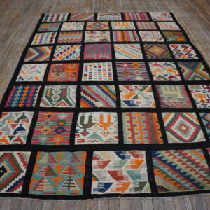 Vibrant, multicolored rug with diverse geometric patchwork squares bordered in black on worn wooden floorboards.
