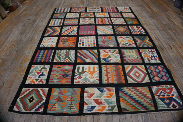 Vibrant, multicolored rug with diverse geometric patchwork squares bordered in black on worn wooden floorboards.