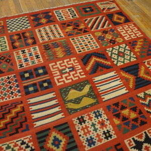 Red flatweave rug with multicolored geometric patchwork and animal motifs on rustic wood flooring.