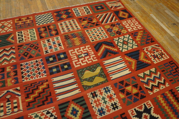 Red flatweave rug with multicolored geometric patchwork and animal motifs on rustic wood flooring.
