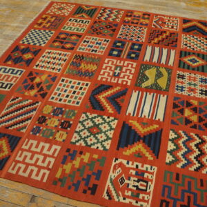 Red-orange flatweave rug with multicolor geometric square panels lying on distressed wooden planks.