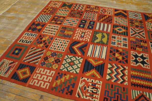Red-orange flatweave rug with multicolor geometric square panels lying on distressed wooden planks.