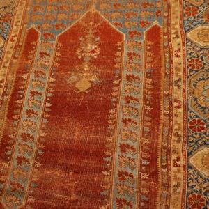 Low-pile red, blue, and tan rug featuring an arch design is displayed on light wooden flooring.