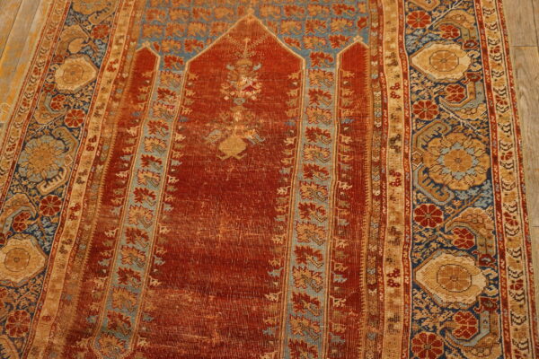 Low-pile red, blue, and tan rug featuring an arch design is displayed on light wooden flooring.