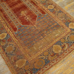 Low-pile rug with a rust red niche field and elaborate gold and blue floral borders on wood planks.