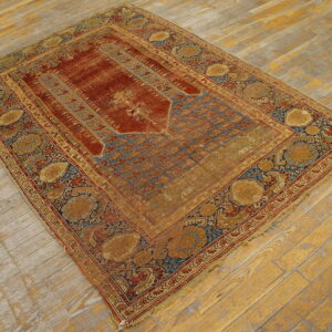 Distressed low-pile rug with red field, blue niche pattern, and wide gold floral borders on wood flooring.