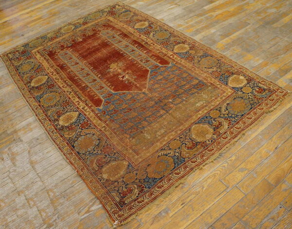Distressed low-pile rug with red field, blue niche pattern, and wide gold floral borders on wood flooring.