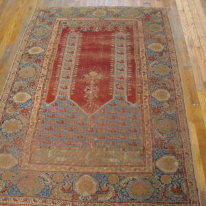 Low-pile, distressed red and blue traditional rug with ornate patterns rests on light wood floors.