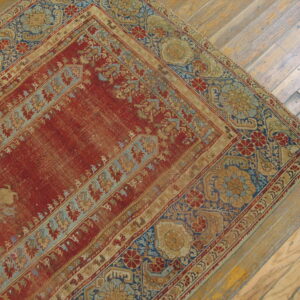 Faded red and blue patterned rug corner on distressed tan hardwood plank flooring.