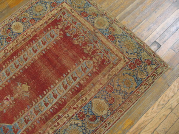 Faded red and blue patterned rug corner on distressed tan hardwood plank flooring.