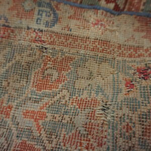 Close-up of a low-pile rug revealing the distressed red and blue pattern with exposed foundation threads.