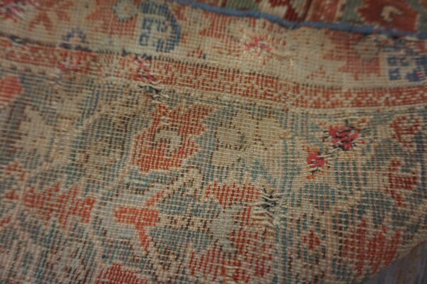 Close-up of a low-pile rug revealing the distressed red and blue pattern with exposed foundation threads.