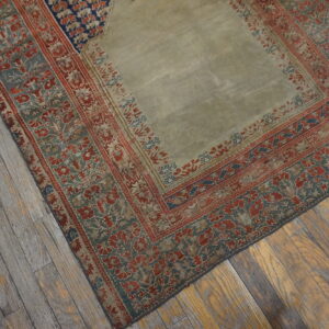 A light green rug with complex red and teal floral borders sits on rustic wood plank flooring.